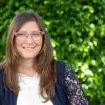 Femme souriante avec des lunettes devant un fond vert.
