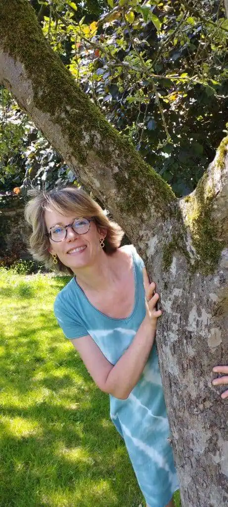 Femme souriante près d'un arbre dans un jardin.